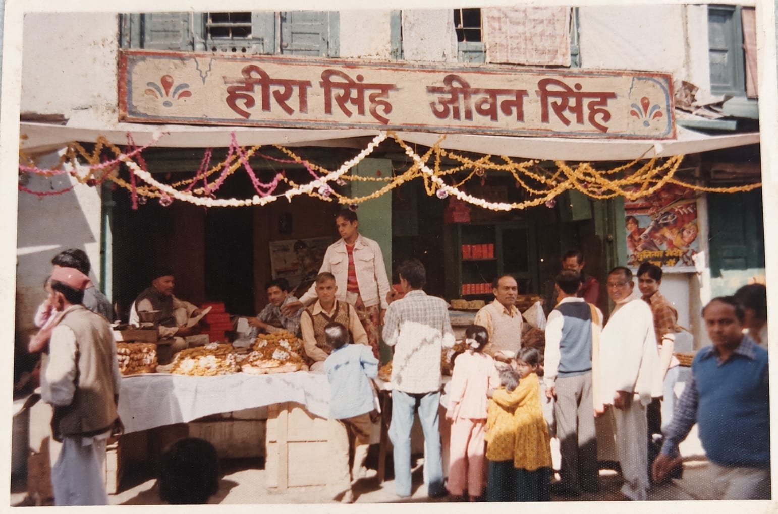 The Heera Singh Jeewan Singh shopfront under its painted signboard, hung with festival garlands and busy with customers