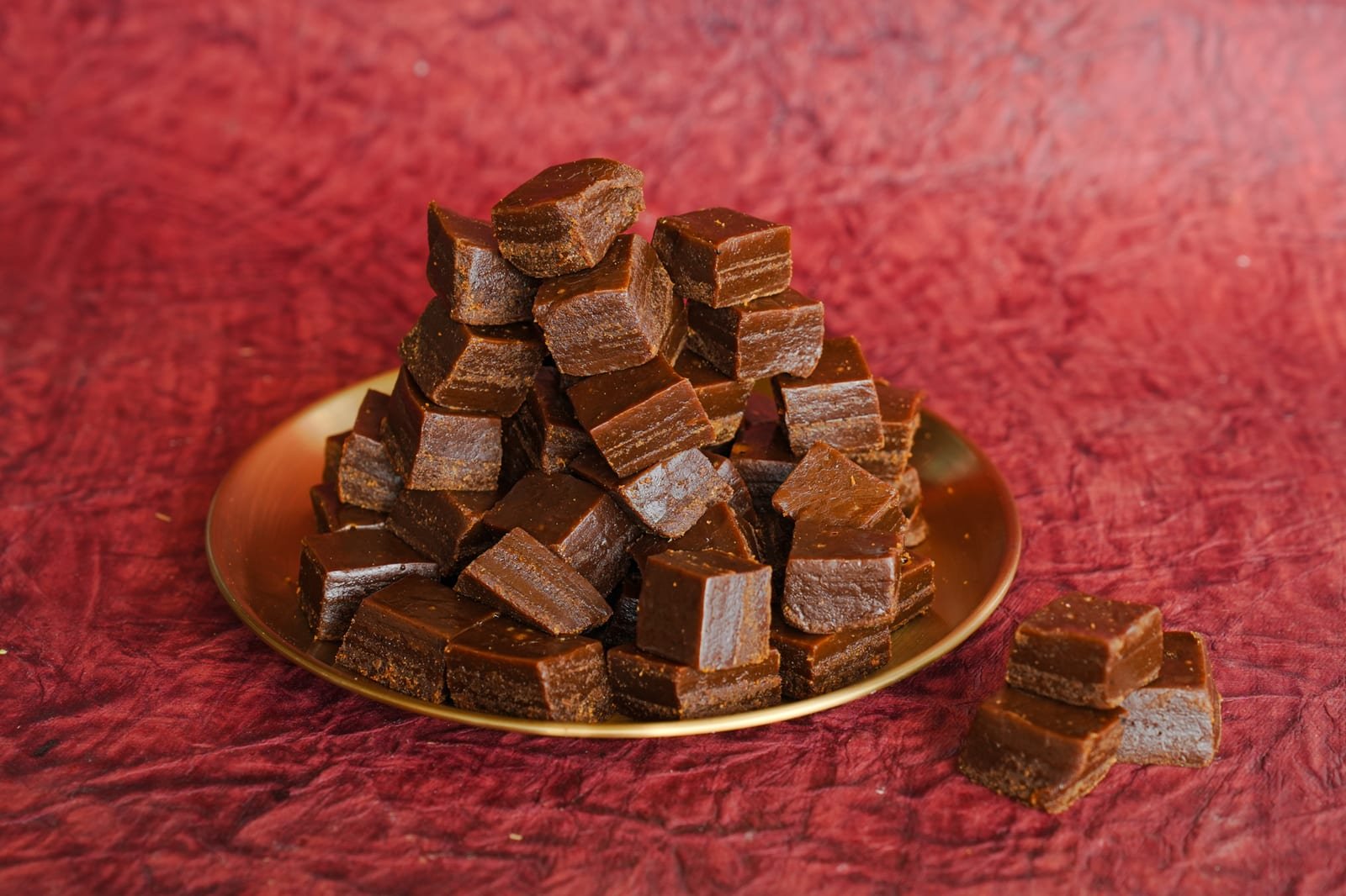 Stacked dark chocolate barfi cut into thick squares on a brass plate